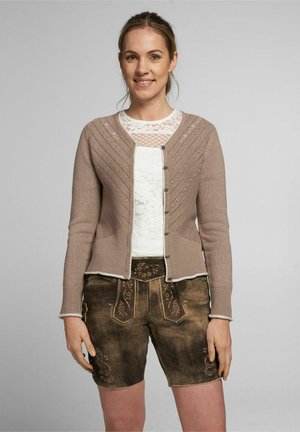 Beige gestrickte Strickjacke mit gemusterter Textur, Knopfverschluss und kontrastierendem weißen Spitzenoberteil, kombiniert mit dunkelbraunen Shorts mit besticktem Design.