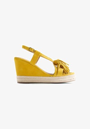 Sandale compensée jaune avec bride à la cheville, semelle en jute tressée et détail pompon sur la bride avant.