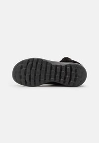 Suela de goma negra con agarre texturizado, que presenta surcos y crestas profundas. Diseño minimalista sin marcas visibles ni adornos.