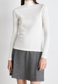 Donna che indossa un top a righe bianche a maniche lunghe e una gonna a scacchi bianco e nero, con un anello d'oro sulla mano destra.