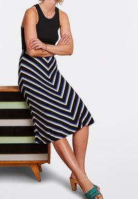 Černý žebrovaný top bez rukávů ve spojení s sukni ke kolenům s modrobéžovými cikcak pruhy. Modelka má na sobě tyrkysové sandály s otevřenou špičkou a podpatkem.