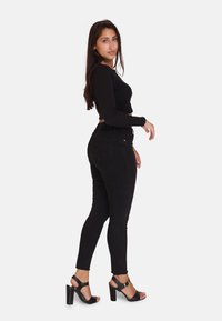 Jeans negros ajustados con una textura suave, cintura alta y diseño clásico. Combinados con sandalias negras de tacón alto con tiras en el tobillo.