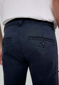 Donker marineblauwe katoenen broeken met een rechte snit, achterzakken met knoopsluitingen en subtiele stiksels. Gladde textuur.