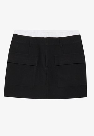 Saia preta feita de tecido entrelaçado, com um cós elástico branco e dois grandes bolsos frontais. Design de corte reto sem padrões.