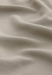 Beige geweven stof met een gladde textuur, voorzien van subtiele horizontale lijnen en natuurlijke vezels, gerangschikt in zachte, vloeiende plooien.