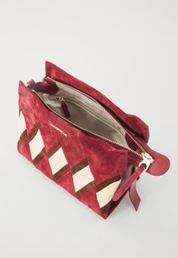 Red suede handbag with a geometric pattern, featuring cream and brown accents, a top zip closure, and a smooth interior lining.