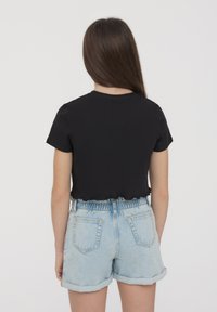 T-shirt nera corta con maniche corte, abbinata a pantaloni corti in denim chiaro con vita elastica e risvolti.