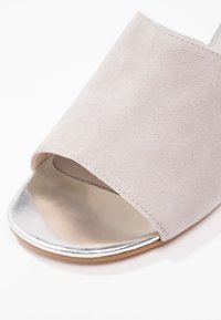 Chaussure en daim gris clair à enfiler, avec un bout ouvert, un avant métallique argenté et une semelle lisse légèrement incurvée.