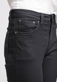 Svarta denimjeans har en standard femficksdesign, dragkedja och subtila sömdetaljer. Tyget har en jämn textur.