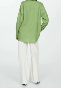 Camisa oversized verde claro hecha de una tela tejida, con mangas largas y dobladillo recto, combinada con pantalones de pierna ancha blancos.