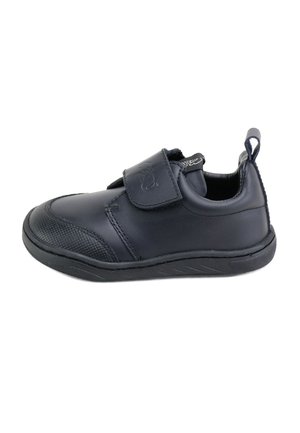 Zapato sintético negro con suela plana, punta redondeada, tira de Velcro, acentos texturizados en la punta y una lengüeta en el talón.