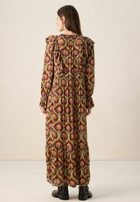 Robe longue à motifs avec épaules volantées, présentant une base bordeaux, un motif floral vert et jaune, et une jupe à volants. Texture du tissu mate.