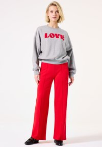Sudadera gris con estampado rojo de "LOVE", combinada con pantalones anchos de tiro alto en rojo con costuras frontales. Unos zapatos negros completan el conjunto.