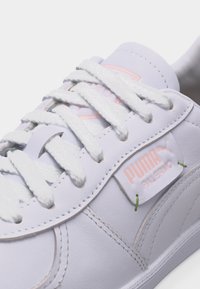 Κοντινό πλάνο λευκού αθλητικού παπουτσιού Puma Palermo με χοντρά λευκά κορδόνια και ροζ λογότυπο Puma στο πλάι και στη γλώσσα του παπουτσιού.