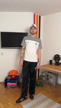 Hvit og grå t-skjorte med kort erm og trykt logo, kombinert med svarte treningsbukser. Svarte joggesko fullfører antrekket.