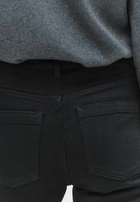 Mustat farkut, joissa on slim fit -leikkaus ja kaksi takataskua. Kangas on sileä ja se on yhdistetty harmaaseen neuleeseen.