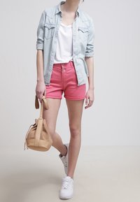 Vaaleansininen farkkupaita valkoisen T-paidan päällä, vaaleanpunaiset shortsit ja valkoiset lenkkarit. Beige, reikäreunainen käsilaukku täydentää rentoa asua.