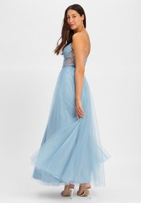 Abito da sera lungo in tulle azzurro chiaro con un corpino decorato di perline, spalline sottili e una gonna fluida, caratterizzato da una texture a strati e scintillante.
