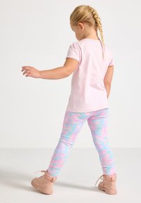 Ružové tričko s krátkym rukávom v kombinácii s farebnými legínami s modro-ružovým vzorom. Hnedé členkové topánky dopĺňajú outfit.