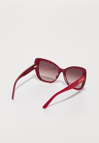 Red heart-patterned sunglasses with dark gradient lenses and solid red arms. Features a subtle logo detail on the arm.