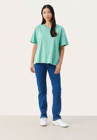 Piparmētru zaļš oversized T-krekls ar īsām piedurknēm, kombinēts ar zilām taisnām biksēm un baltām kedām. Minimālistisks dizains un brīvs piegriezums.