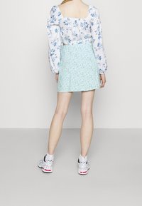 Bílá květinová blůza s dlouhým rukávem a čtvercovým výstřihem, v kombinaci s mentolově zelenou sukní s malým květinovým potiskem. Bílé sportovní tenisky.