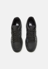 Black athletic shoes with a smooth leather upper, perforated toe, round laces, and embossed detailing on the sides. Flat rubber sole.