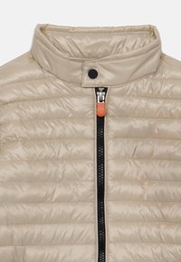 Beige puffer jacket with a standing collar, zip closure, and contrasting orange zipper pull. Features horizontal quilting and a smooth finish.