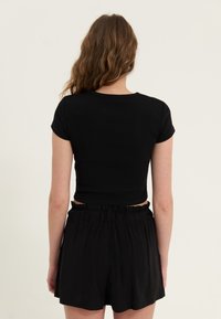Czarny prążkowany top z krótkim rękawem, zestawiony z czarnymi szortami na elastycznej talii, widziany z tyłu na neutralnym tle.