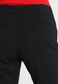 Zwarte broek met een gladde textuur, een getailleerde snit en twee achterzakken met een minimalistisch ontwerp. Geen zichtbare hardware of patronen.