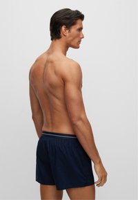 Navy swim shorts in lightweight material with elastic waistband and a white accent. View shows a man from the side, highlighting the back design.