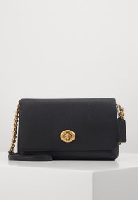 Sac à main en cuir noir avec finition texturée, quincaillerie en logo doré, anse en chaîne et en cuir, forme rectangulaire, fermeture à rabat et étiquette attachée.