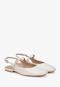 Płaskie buty slingback w błyszczącej kremowej lakierowanej skórze. Posiadają okrągły czubek, wycięcia po bokach oraz mały obcas w bloku z metalowymi elementami w kolorze srebrnym.