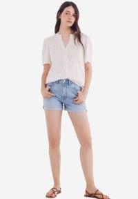 Witte, loszittende blouse met een v-hals en korte mouwen, gedragen met lichtblauwe denim shorts met opgerolde zomen en zakken.