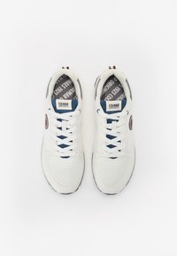 Vita sportskor i vitt med mesh och syntetiskt material. Blå accenter på tungan och snörena, med en rund logotyp-patch och strukturerade sulor.