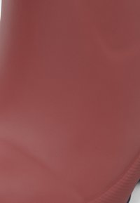 Primo piano di una superficie rossa liscia e opaca con ombre sottili e una leggera cucitura diagonale sul bordo destro.