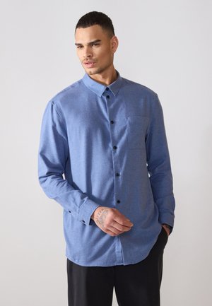 Camisa azul de manga larga con botones, hecha de tela texturizada, con botones negros y un bolsillo en el pecho, de corte relajado y dobladillo redondeado.