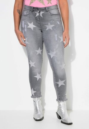 Graue Denim-Jeans mit großen hellgrauen Sternmustern, ausgefransten Säumen und verzierten Details. Kombiniert mit silbernen Ankle-Boots.
