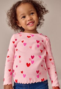 Lyserød ribbet langærmet skjorte med spredte røde og lyserøde hjerte mønstre. Skåret sømkant, der komplimenterer en afslappet stil.