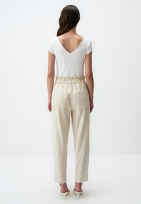 Haut blanc à manches courtes côtelé avec col en V, associé à un pantalon beige à coupe décontractée avec une taille élastique et des poches latérales.