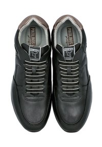 Zapatillas de cuero negro con acentos marrones, que presentan un diseño elegante, una superficie texturizada y cordones elásticos para fácil uso. Etiqueta de Pikolinos visible.