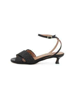 Sandalo nero con tacco basso, cinturini intrecciati anteriori, cinturino alla caviglia con fibbia e soletta imbottita beige su sfondo bianco.