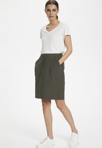 Kakifärgad elastisk midjeskirt med sidofickor, knälång, ihop med en vit t-shirt med V-ringning och vita sneakers. Slät textur, avslappnad design.