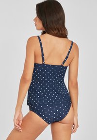 Tankini de lunares en azul marino con tirantes ajustables, torso ajustado y dobladillo suelto. Parte inferior de cintura alta a juego con el mismo patrón.