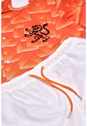 Oranž kirikuga särg, millel on geomeetriline muster ja must lõvi logo. Valged lühikesed püksid oranžiga paelaga. Tekstuuriga kangas.