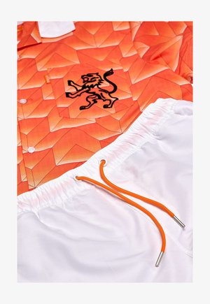 Oranž kirikuga särg, millel on geomeetriline muster ja must lõvi logo. Valged lühikesed püksid oranžiga paelaga. Tekstuuriga kangas.