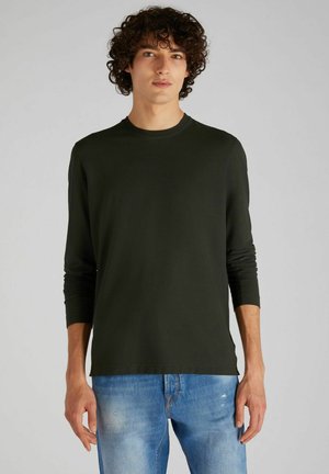 Dark green long-sleeve shirt with a round neck and fitted sleeves. The fabric appears smooth, paired with light blue distressed jeans.