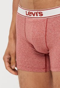 Crvene muške bokserice od čempresa s belim elastičnim pojasom na kojem piše "Levi's". Napravljene od mekog, rastezljivog materijala s detaljima šavova.