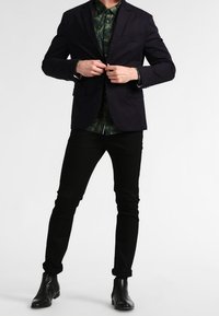 Navy blazer over a green leafy patterned shirt, paired with black slim-fit trousers and black leather ankle boots. Standard fit and color palette.