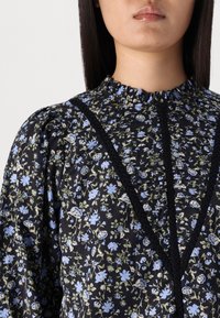 Abito nero floreale con motivi blu chiaro e verdi, con un collo arricciato e dettagli in nero, in tessuto morbido e maniche voluminose.